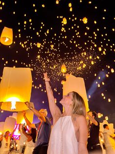 a woman in a white dress is holding up some paper lanterns as others look on