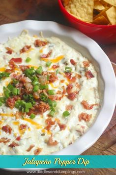 a bowl of dip with bacon, cheese and green onions next to some tortilla chips