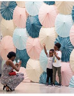 a woman kneeling down next to a little boy in front of an umbrella wall with blue and pink umbrellas on it