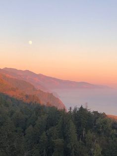 the sun is setting over some mountains with trees on each side and fog in the air