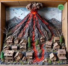 a cardboard box with a volcano in the middle and small houses on the bottom that have lava coming out of it