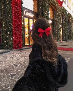 a woman walking down the street with a red bow in her hair and wearing a black coat