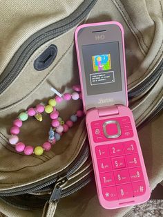 a pink cell phone sitting on top of a bag next to a beaded necklace