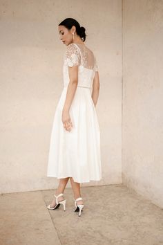 a woman in a white dress and high heeled shoes is standing against a wall