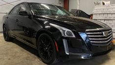 a black cadillac parked in a garage next to stacks of boxes and pallets on the floor