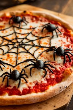 a pizza topped with cheese and black spider web toppings on a wooden cutting board