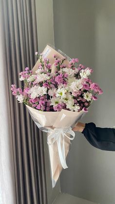 a person holding a bouquet of flowers in front of a window with curtains behind them