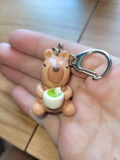 a hand holding a small plastic bear keychain with an egg in it's mouth