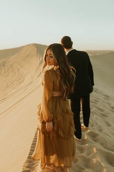 a man and woman walking in the sand dunes