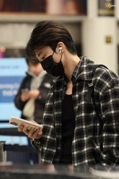 a man wearing a face mask while looking at his cell phone in an airport terminal