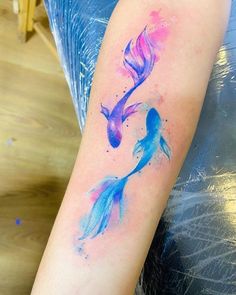 watercolor tattoo on the arm of a woman with blue and pink fish in it