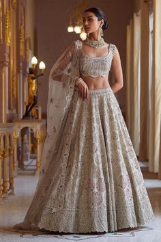 a woman in a white and gold lehenga stands on the floor with her hands behind her back