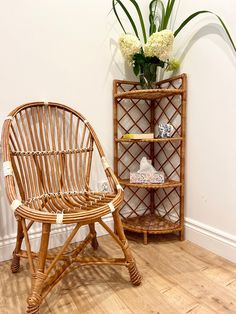 a wicker chair next to a bamboo shelf with flowers in it and a vase on top