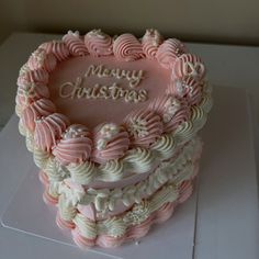 a pink and white decorated cake with merry christmas written in frosting on it's side