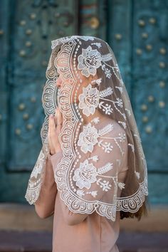 a woman wearing a veil and praying in front of an ornate blue door with flowers on it