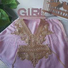 a pink shirt with gold embroidered details on the chest and shoulder, next to a bird cage