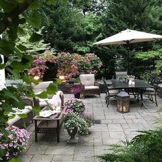 a patio with tables, chairs and umbrellas in the middle of it surrounded by flowers