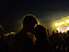 two people standing in front of a crowd at a music festival with bright lights on the stage behind them