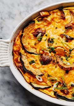 a casserole dish with eggplant, sausage and onions in it on a marble surface