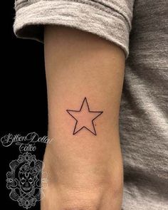 a small star tattoo on the left inner arm, with an inscription in black ink