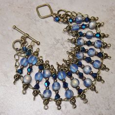 "Beaded bracelet drapes gracefully over your wrist with a mix of cobalt blue AB bi cone crystal beads and round blue glass beads accented with antique brass beads. Wire wrapped segments of beads are linked on antique brass chain. Bracelet closes with a matching antique brass metal toggle closure. This bracelet has a slinky fit and the blue beads have a brilliant AB quality to them. Length of the bracelet is 7 1/2\" (19.5 cm) and the width is 1 1/4\". Let me know prior to shipping if you need an Bohemian Blue Czech Glass Bracelets, Blue Czech Glass Bracelets With Spacer Beads, Blue Wire Wrapped Bracelets With Round Beads, Blue Wire Wrapped Bracelet With Round Beads, Blue Wire Wrapped Beaded Bracelets, Adjustable Blue Bohemian Chain Bracelet, Adjustable Blue Round Bead Chain Bracelet, Adjustable Blue Chain Bracelet With Round Beads, Blue Bohemian Beaded Bracelets With Dangling Beads