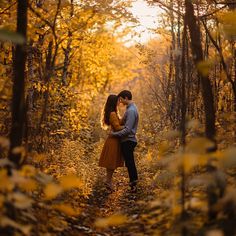 a couple embracing in the woods surrounded by trees with yellow leaves on them and one man is kissing the woman's forehead