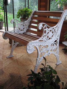 a wooden and white bench sitting in front of a glass wall with potted plants