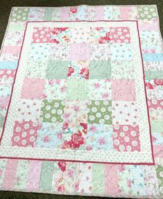 a pink and green patchwork quilt with flowers on the front, sitting on carpet