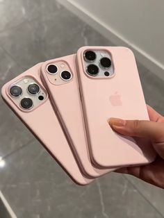 three pink iphones are being held up in front of the camera, and one is holding