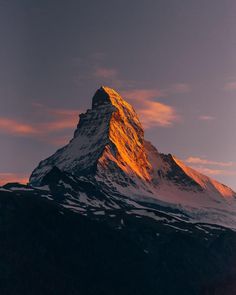 a snow covered mountain with the sun shining on it's peak and clouds in the background