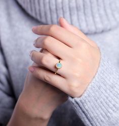 a woman's hand wearing a gold ring with a white stone