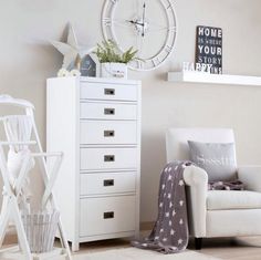 a living room with white furniture and a clock on the wall above it's drawers