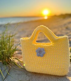 a crocheted yellow purse sitting on top of a sandy beach next to the ocean