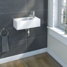 a white sink sitting next to a window on top of a wooden floor in a bathroom