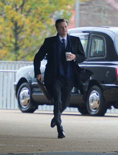 a man in a suit and tie walking down the street with a cup of coffee