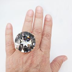 a person's hand holding a ring with a large diamond in the middle of it