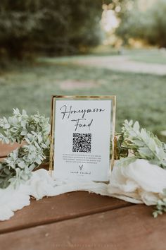 a sign that is sitting on top of a table with flowers and greenery around it