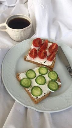 two slices of bread with cucumbers and tomatoes on them next to a cup of coffee