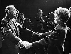 black and white photograph of two people shaking hands in front of other people wearing suits