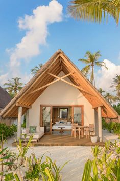 a small white house with a thatched roof on the beach near palm trees and blue sky