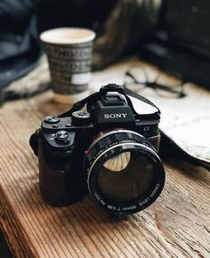 a black camera sitting on top of a wooden table next to a cup of coffee