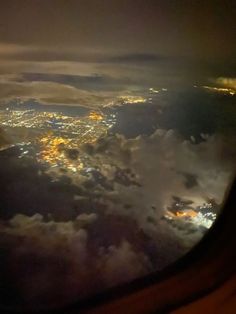 the view out an airplane window at night from above, looking down on clouds and city lights