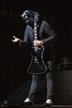 a man with a guitar in his hand and a black mask on top of him