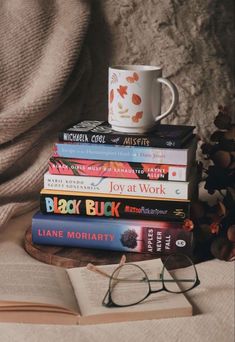 a stack of books and glasses on top of a blanket next to a cup with coffee