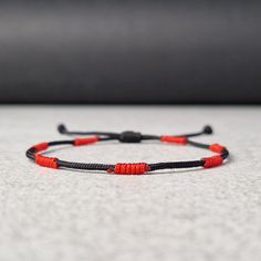 a red and black string bracelet with two beads on it sitting on a white surface