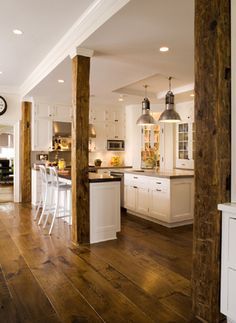 an open kitchen and dining room with wood floors, white cabinets and wooden beams in the ceiling