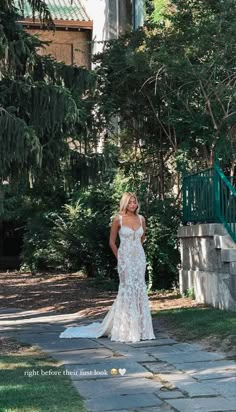 a woman in a white wedding dress standing on a stone walkway with trees and bushes behind her