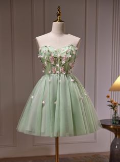 Frolic with grace at your homecoming in this delicately crafted mint green dress that whispers tales of spring! It's a vision of loveliness with its hand-embroidered bodice, where each cherry blossom seems to come alive in a symphony of pinks and greens. The dress boasts a playful sweetheart neckline, inviting admiration and sweet memories. Below the waist, the full skirt blooms like a meadow, with tulle layers that add an air of lightness and joy. Tiny floral accents are sprinkled across the skirt, catching the light and the gaze of onlookers. This dress isn't just a choice for homecoming; it's a promise of a magical evening wrapped in beauty and splendor. Green Short Prom Dress, Dress Green Short, Homecoming Dresses Green, Party Dress Green, Beaded Party Dress, Cute Homecoming Dresses, Green Homecoming Dresses, Floral Prom Dresses, Green Tulle