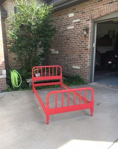 a red metal bed frame sitting in front of a brick building