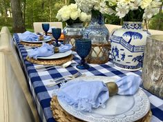 a blue and white table setting with flowers in vases on the side, plates and utensils